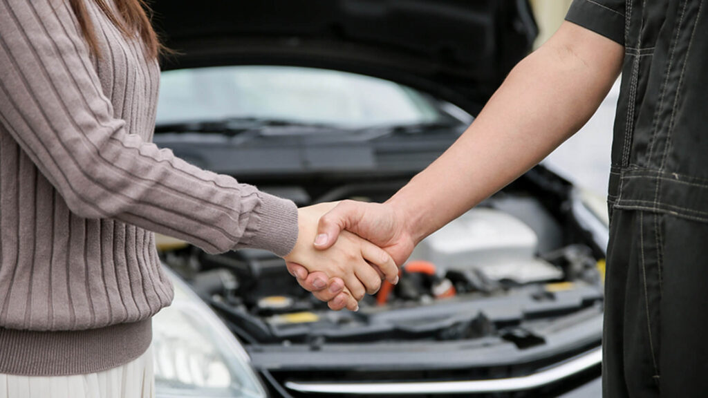 自動車のボンネットを開けた状態で、整備スタッフとお客様が握手を交わしている様子