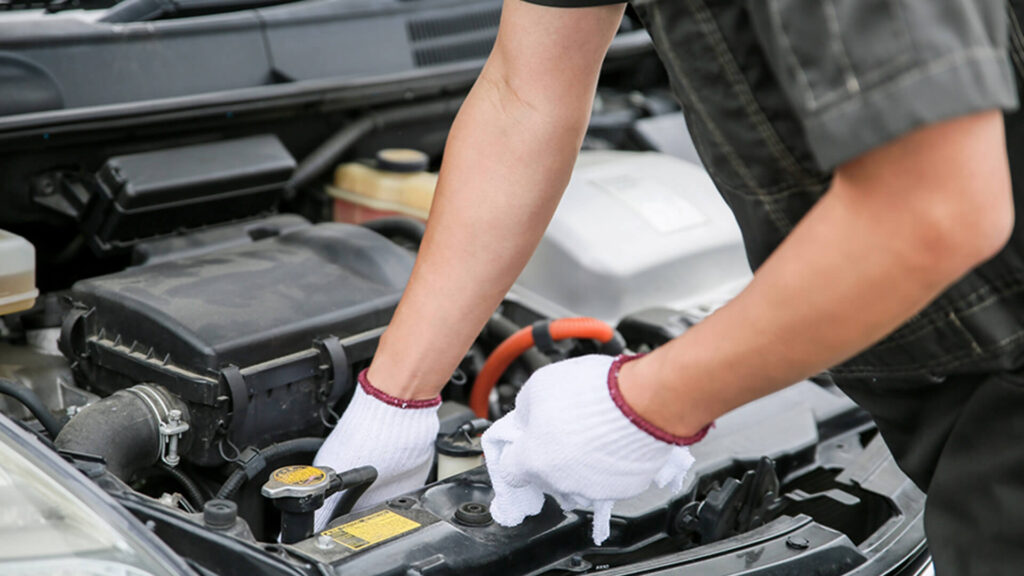 白い軍手を着用した整備士が、車のエンジンルームを丁寧に点検・清掃している様子