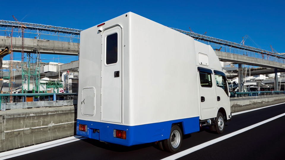 路上に停車したヴィオン製の白と青のツートンカラーの自走式トイレカー。